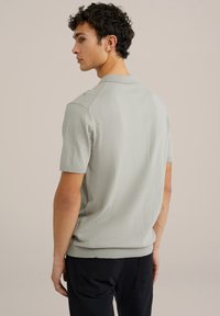 Polo de culoare gri deschis, cu mânecă scurtă, cu un design texturat pe umeri, guler clasic și o croială ajustată, fabricat dintr-un material moale, tricotat.