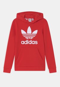 Röd hoodie i mjukt material med en stor vit adidas-logga och tre horisontella ränder. Inkluderar en kenguruficka och ribbade ärmslut.