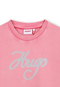 Różowy sweter z okrągłym dekoltem i żebrowanym wykończeniem oraz srebrnym haftowanym logo "Hugo" z przodu. Miękka tekstura tkaniny, casualowy design.