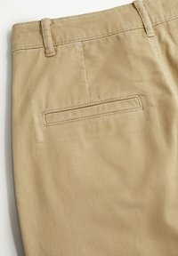 Beige Baumwollhosen mit glatter Textur, tailliertem Schnitt und einer einzelnen Gesäßtasche mit gestickten Details.