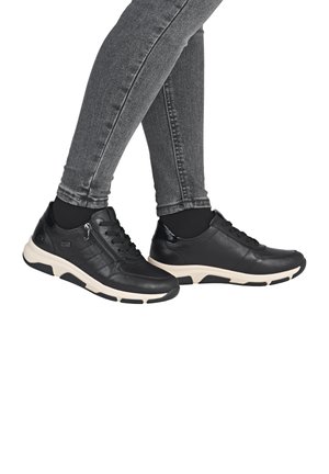 Baskets en cuir noir avec une semelle crème, présentant un laçage, une fermeture éclair latérale et des accents texturés, mises en valeur sur un jean gris.