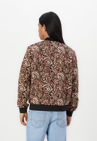Bomberjack in een paisleypatroon in bruin, rood en wit. Zachte stof, ribgebreide manchetten en zoom, en een zwarte kraag. Casual ontwerp.
