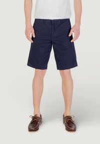 Pantaloni corti blu navy realizzati in tessuto leggero, con davanti piatto, passanti per cintura e orlo rifinito. Scarpa da barca marrone con lacci.