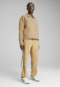 Beige Hose mit weißen Seitenstreifen, kombiniert mit einem hellbraunen Hemd mit vertikalen Streifen. Dazu weiße Sneaker mit grünen Akzenten.