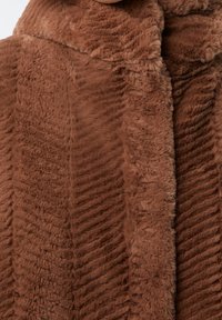 Tessuto marrone, morbido e peloso, con una texture a coste, caratterizzato da un colletto finto e cuciture che creano un aspetto strutturato. Materiale morbido e accogliente.
