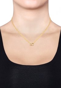 Collier en or avec un pendentif en symbole de l'infini minimaliste, présentant une finition lisse et une texture tissée. Design simple adapté à l'empilement.