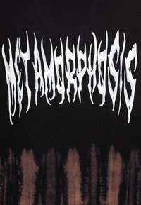 Svart tyg med en tie-dye gradient som övergår till brunt i botten. Har stor, förvriden vit text som säger "METAMORPHOSIS."