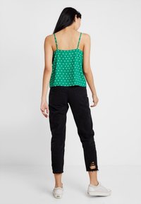 Camisola verde a pois con spalline regolabili, abbinata a jeans neri strappati. L'outfit è completato da sneakers bianche.