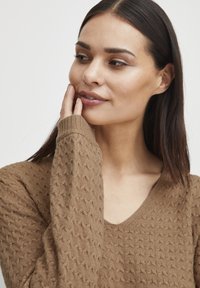 Pull en maille marron avec un motif texturé, design en V et manches longues. Matière douce et détails subtils sur la surface du tissu.