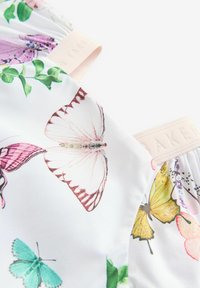 Tessuto bianco con stampe colorate di farfalle e fiori. Materiale morbido e leggero con un'etichetta in elastico rosa.