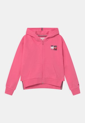 Haut zippé rose en coton doux. Présente un patch logo graphique sur la poitrine, des poches kangourou et des poignets côtelés.