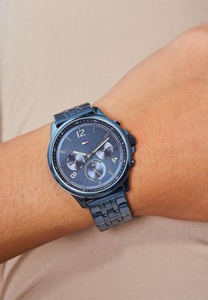 Reloj cronógrafo metálico azul con un dial texturizado azul, acentos plateados, tres subdiales y una pulsera de eslabones. Lleva puesto en la muñeca sobre el tono de piel.