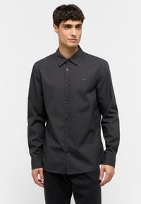 Camisa de manga larga negra hecha de tela suave, con cuello también de botón, botones en la parte frontal y un pequeño logotipo bordado en el pecho.
