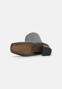 Botte cheville en cuir noir avec un bout arrondi, dotée d'une semelle en caoutchouc marron texturée et d'un petit talon. Aucun motif ou accent visible.