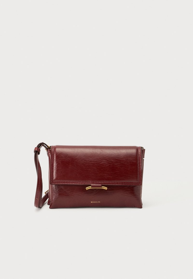 Σκούρα κόκκινη δερμάτινη τσάντα crossbody με μπροστινό καπάκι, χρυσό κούμπωμα και ρυθμιζόμενο ιμάντα ώμου σε μονόχρωμο φόντο.