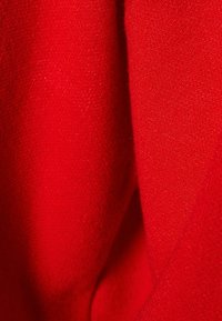 Nahaufnahme von rotem Stoff, der eine weiche Textur mit glatter Oberfläche aufweist. Das Material scheint leicht faserig zu sein und zeigt eine gleichmäßige Farbausgabe.