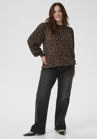 Schwarz- und braun gemusterte Bluse mit langen Ärmeln und elastischen Bündchen, kombiniert mit dunklen weit geschnittenen Jeans und spitzen schwarzen Ballerinas.