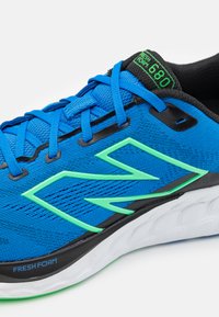 Blauwe hardloopschoen met textuurstof bovenkant, zwarte accenten, groene logo en Fresh Foam demping. Kenmerkt vlakke veters en gestructureerde tong.