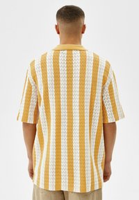 Korte mouwen shirt met een geometrisch patroon, voorzien van afwisselende gele en witte strepen. Gebreide textuur, klassieke kraag, casual pasvorm.