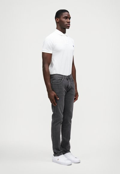 Camiseta polo branca, jeans cinza de corte slim e ténis brancos. A polo tem uma gola curta, detalhes sutis de logo e uma textura de tecido suave.