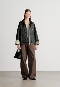 Roheline veekindel jope pruunide krae ja triibuliste mansettidega, ees kaks taskut. Sobitatud pruunide laiade pükstega ja väikese musta kotiga.