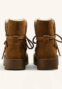 Hnedé semišové členkové čižmy s mäkkou kožušinovou podšívkou, šnurovací dizajn a hrubá hnedá gumená podrážka. Hladká textúra s klasickým siluetou.