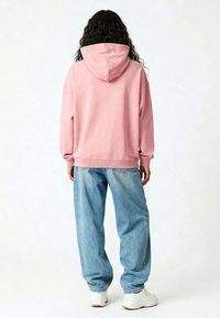 Felpa rosa con cappuccio regolabile, polsini e orlo a costine. Abbinata a jeans baggy azzurri chiari e sneakers bianche.