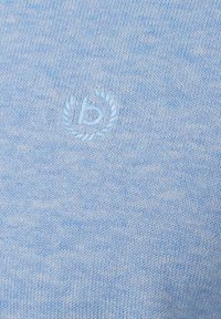 Himmelblaues Strickgewebe mit subtil gesticktem, kreisförmigem Logo, das ein kleines "b" zeigt, umgeben von Lorbeerblättern.