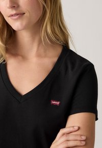 Schwarzes Baumwoll-V-Ausschnitt-T-Shirt mit einem kleinen, roten Levi's-Logeanhänger auf der linken Seite, mit kurzen Ärmeln und einem lässigen Schnitt.