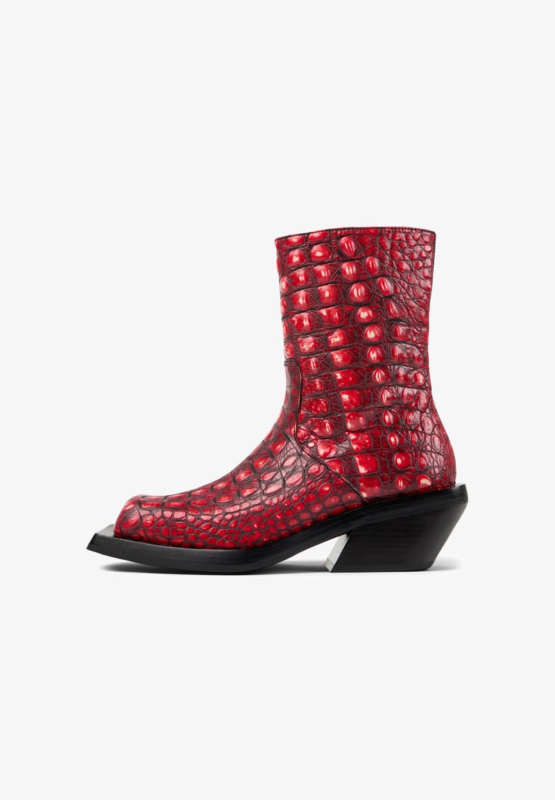 Bottine rouge à la texture croco brillante avec un talon noir épais et incliné, vue de profil sur fond blanc.