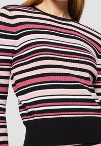 Pull en tricot côtelé avec des rayures horizontales en rose, noir et blanc. Encolure ronde et manches longues. Coupe slim avec un ourlet noir.