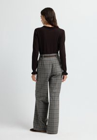 Bruine langemouwen top met een gerimpelde halslijn, gecombineerd met ruime gestreepte broek in grijs, bruin en crème. Inclusief een bruine riem.