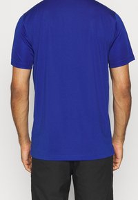 T-shirt bleu à manches courtes, texture lisse, coupe ajustée. Présente un col rond et un ourlet droit, vu de dos.