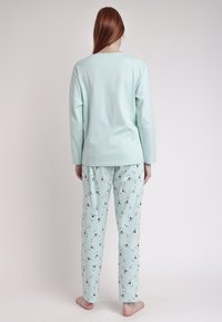 Conjunto de pijama de algodón de un suave verde menta que incluye una camiseta de manga larga y pantalones estampados con pingüinos y copos de nieve en blanco y negro.