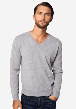 Hellgrauer V-Ausschnitt-Pullover aus weichem Stoff mit langen Ärmeln, gerippten Bündchen und Saum; kombiniert mit dunkelblauen Jeans.