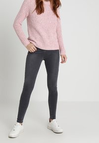 Ciemnoszare obcisłe dżinsy z denimu, zestawione z jasnoróżowym swetrem o fakturze i białymi trampkami. Minimalistyczny design bez wzorów.