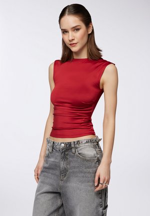 Top rosso senza maniche con una silhouette aderente e dettagli arricciati, abbinato a jeans a gamba larga grigio chiaro a vita alta.