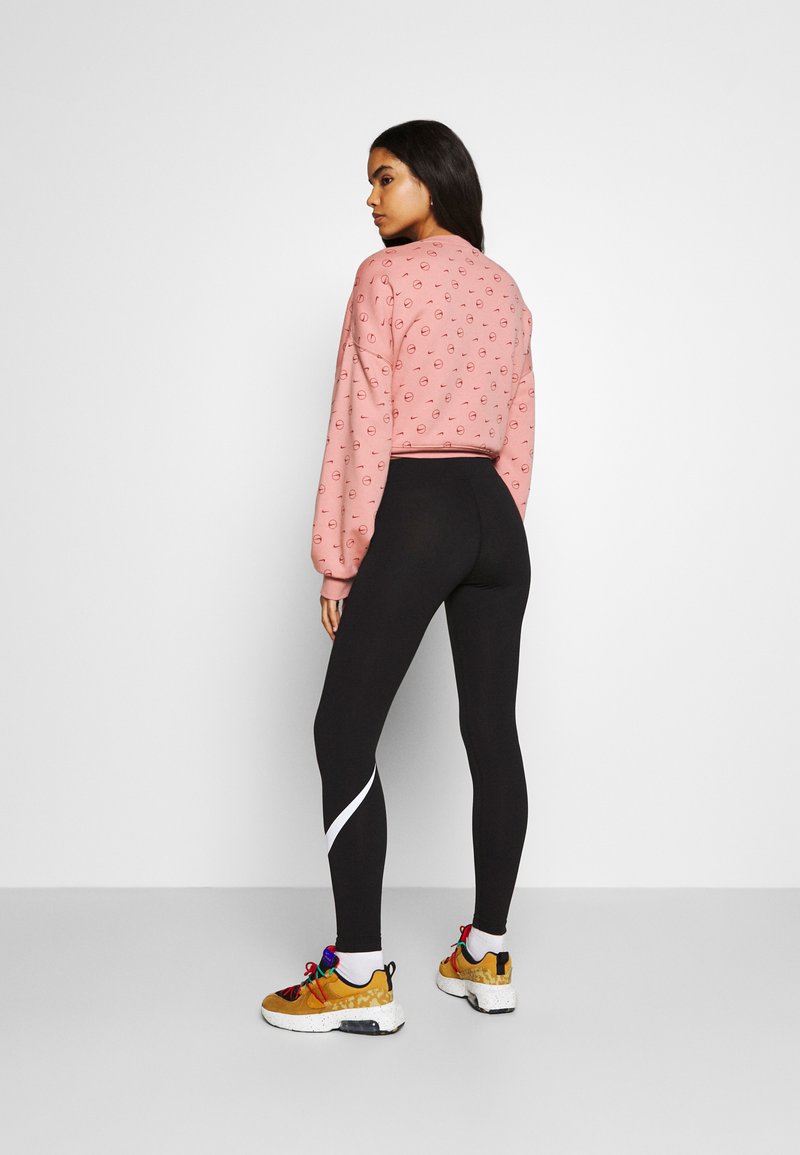 Sweat-shirt rose coupé avec petits logos, leggings noirs avec bande blanche sur les côtés, et baskets multicolores avec semelles texturées.