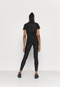 Czarny t-shirt z krótkim rękawem połączony z czarnymi legginsami. Legginsy mają gładką strukturę, a stylizację dopełniają czarne trampki.