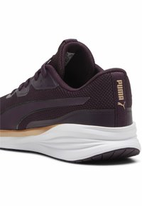 Zapatilla deportiva púrpura con parte superior de malla, suela de goma y collar acolchado. Presenta un detalle de logo dorado y acentos texturizados en los laterales.
