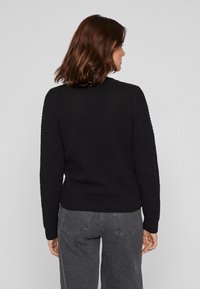 Μαύρος υφασμάτινος πουλόβερ με στρογγυλή λαιμόκοψη, ριμπ στρίφωμα και μακριά μανίκια, συνδυασμένο με γκρι παντελόνι ψηλής μέσης.