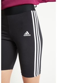 Czarne spodenki sportowe z wysokim stanem, z trzema białymi pionowymi paskami po bokach i małym białym logo Adidas.