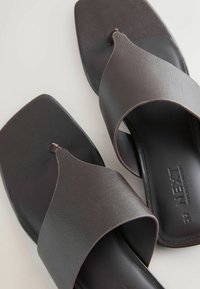 Paie de sandales noires slip-on avec larges brides et bout carré, en matériau synthétique texturé avec le logo "NEXT" sur la semelle intérieure.