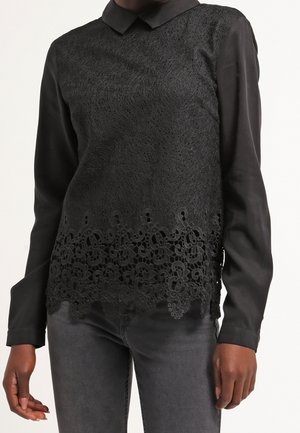 Czarna bluzka z długim rękawem z koronkową nakładką i kwiatowym wycięciem u dołu, zestawiona z ciemnoszarymi jeansami.
