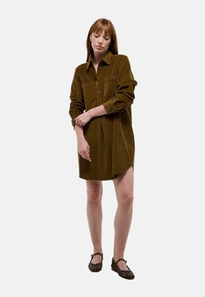 Robe chemise en velours côtelé vert olive avec un devant à boutons, des manches longues, deux poches poitrine et des fentes latérales. Associée à des ballerines marron à motifs.