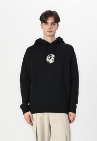 Μαύρη κουκούλα φούτερ με μπροστινή τσέπη και κρεμ έμβλημα yin-yang στο στήθος. Κατασκευασμένη από υλικό φλις με ριμπ στις μανσέτες και στη μέση.