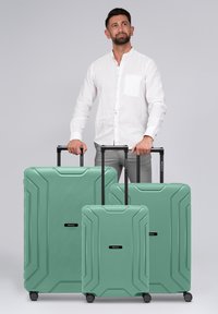 Tres maletas duras verdes de diferentes tamaños con un patrón texturizado y asas de tiro negras, con ruedas y logotipo de la marca.
