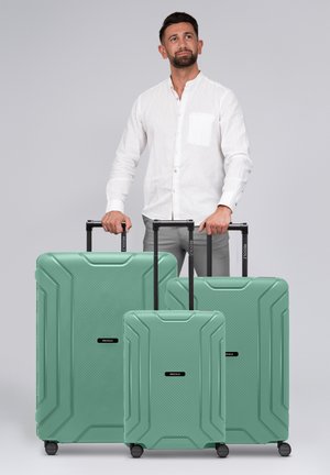 Drie groene harde koffers van verschillende maten met een textuurpatroon en zwarte trekhandvatten, uitgerust met wieltjes en een merklogo.