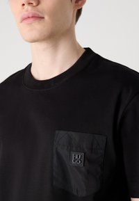 Czarna koszulka z ribbowanym okrągłym dekoltem, z teksturowaną czarną kieszenią w diamentowy wzór i wytłoczonym detalem logo.