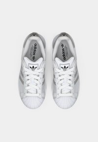 Pair of white Adidas sneakers with gray stripes, white laces, and shell toe design, viewed from above on a white background.